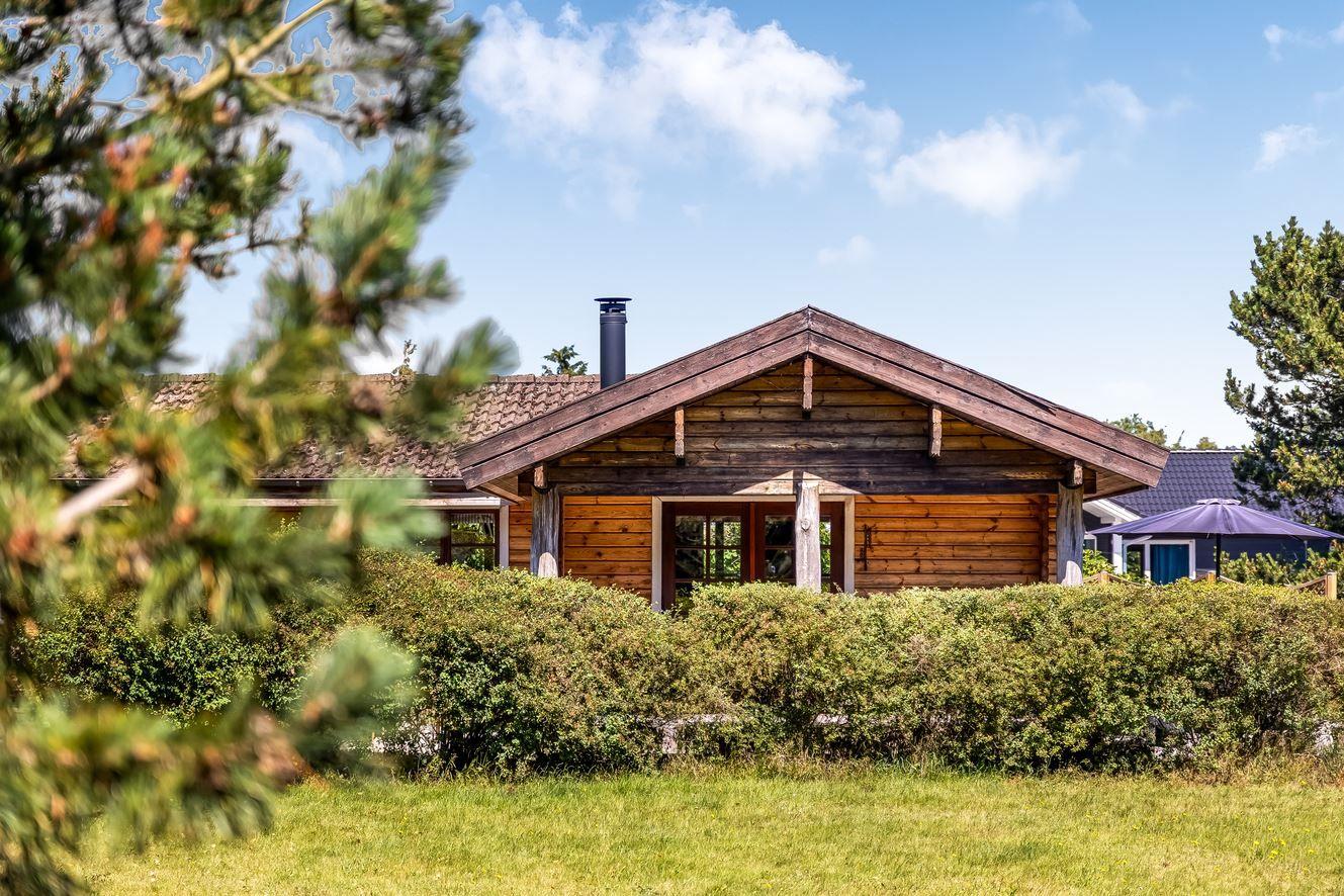 Holzhaus mit Dach und Schornstein hinter Hecke und Bäumen
