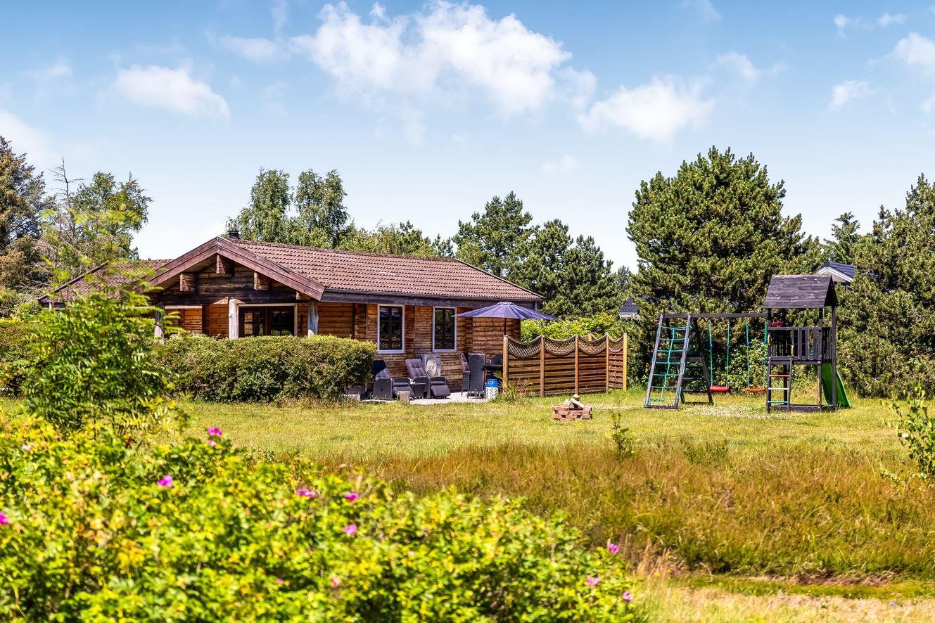 Holzhäuschen mit Garten, Spielplatz und Sitzgelegenheiten.