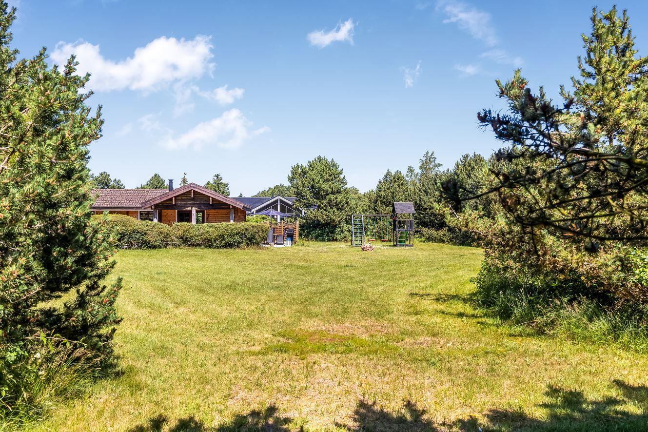 Holzhäuser mit großem Garten und Spielplatz unter blauem Himmel.