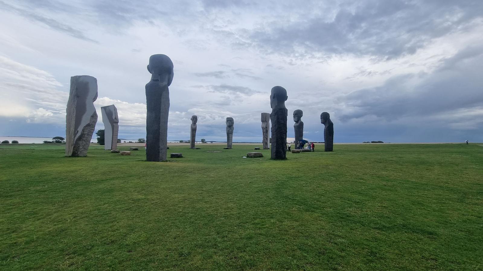 Grünes Feld mit steinernen Skulpturen unter bewölktem Himmel