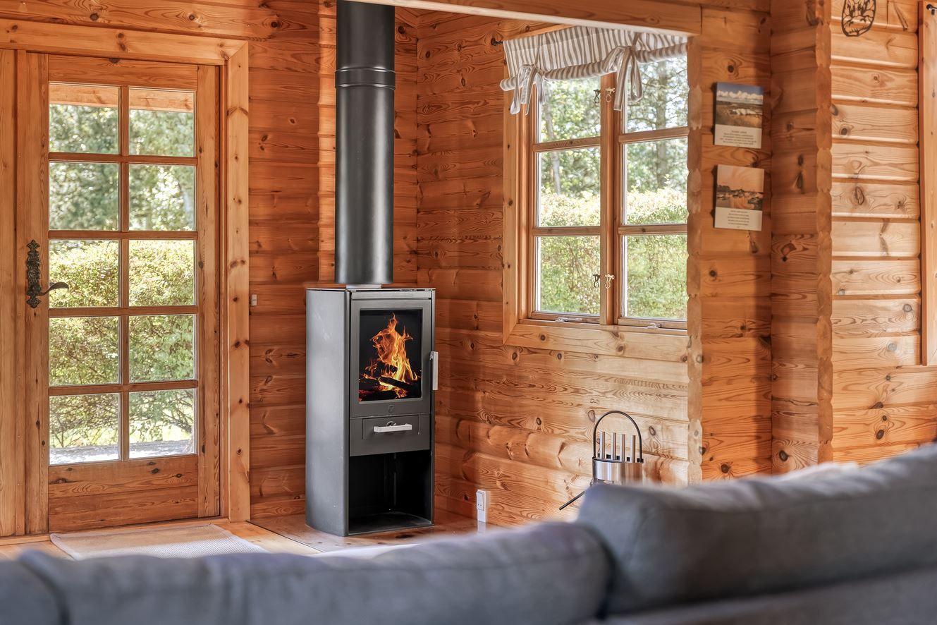 Holzhaus mit Kamin, Fenster und Tür. Sofa im Vordergrund.