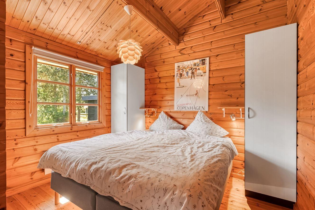 Schlafzimmer mit Holzwänden, Bett, Fenster und weißen Schränken.