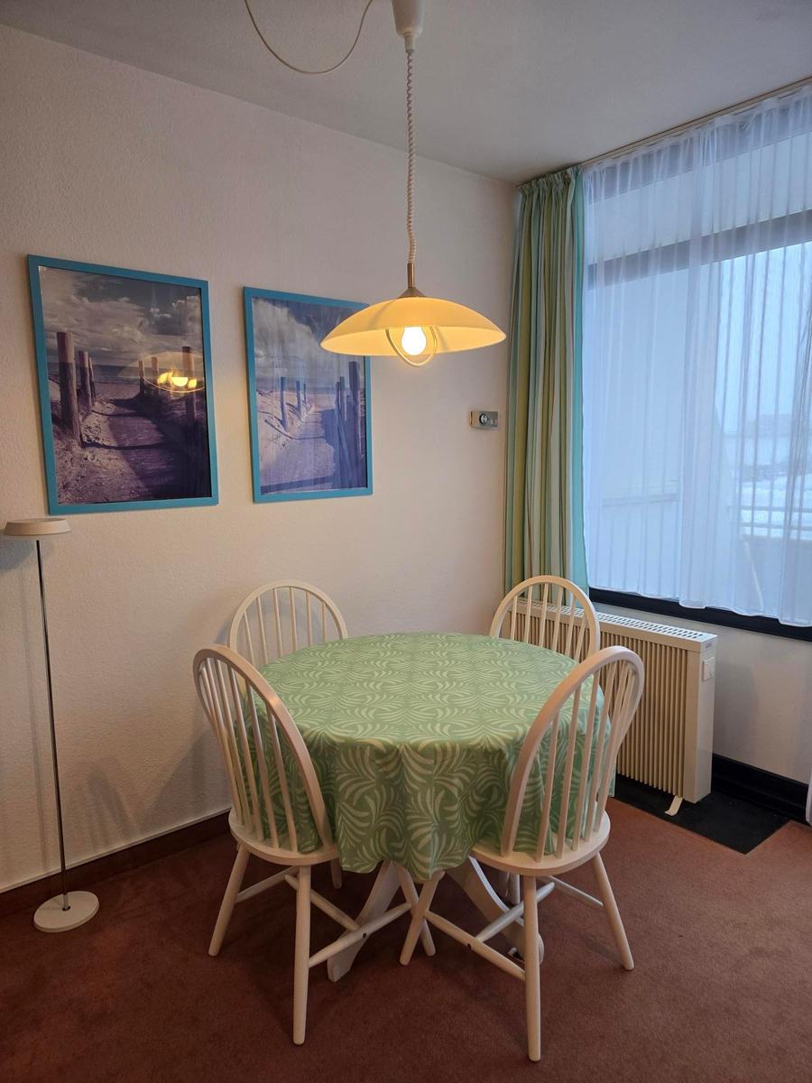 Rundtisch mit vier Stühlen, grüne Tischdecke, Fenster mit Vorhängen.