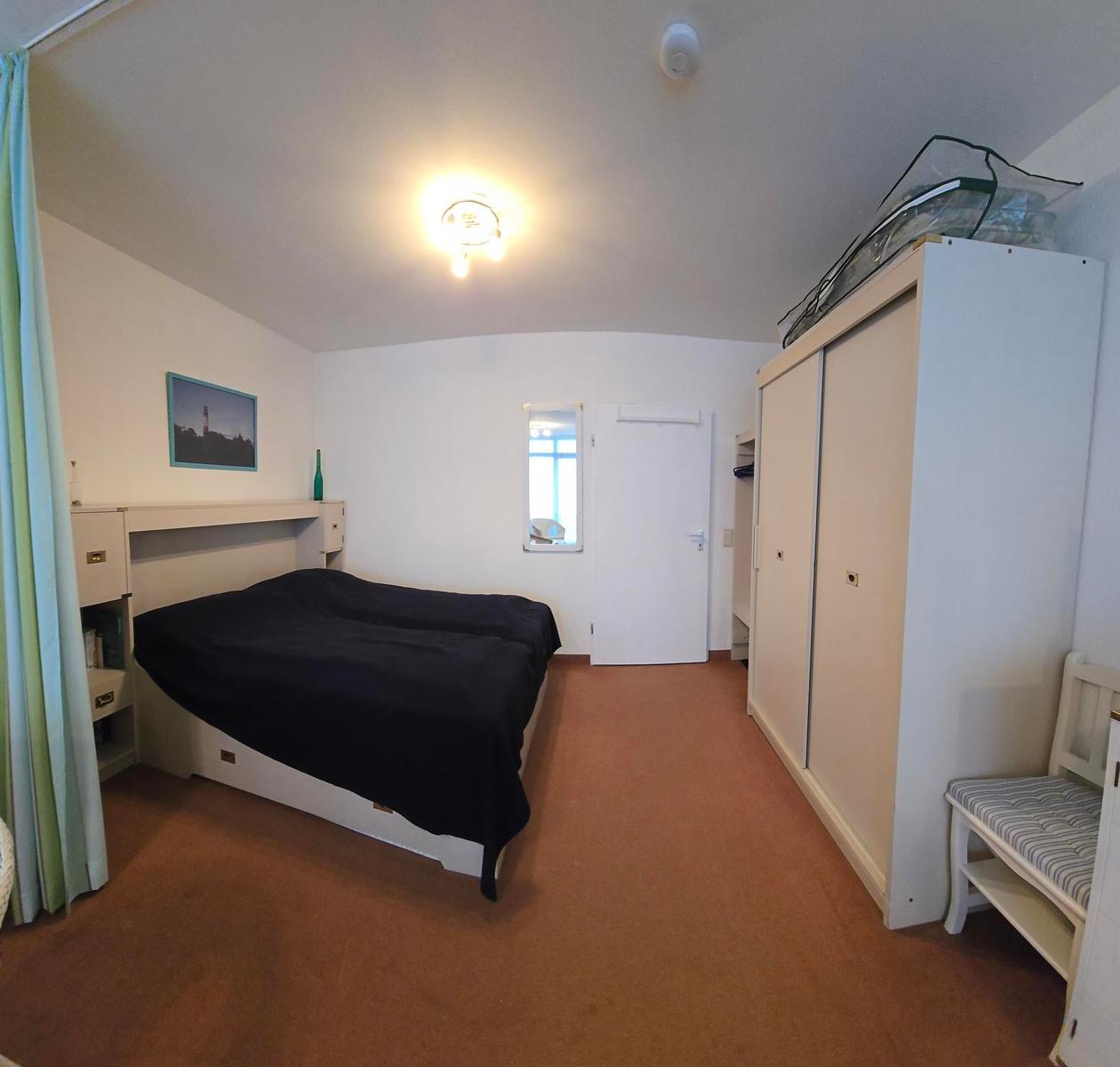 Schlafzimmer mit Bett, Kleiderschrank und Stuhl.