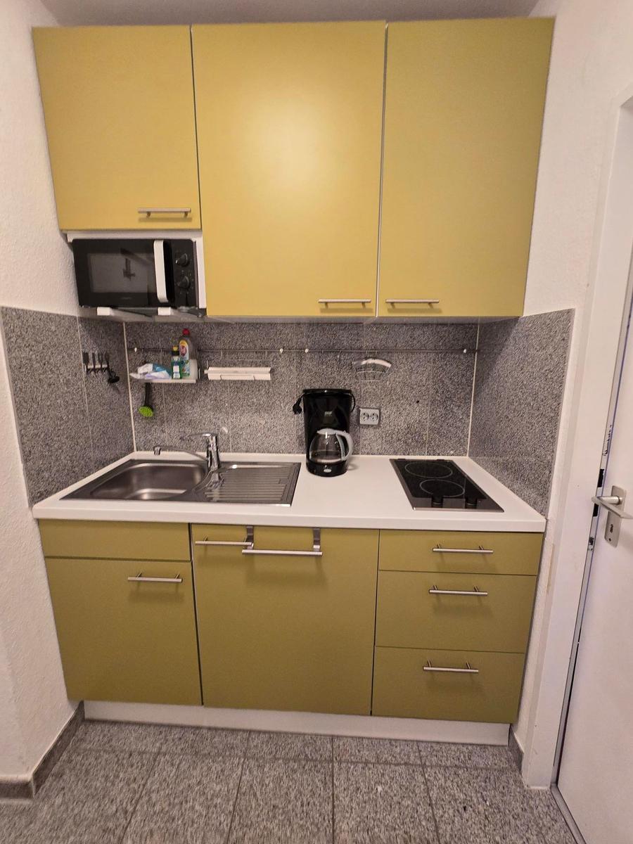 Küche mit gelben Schränken, Herd, Spüle und Mikrowelle.