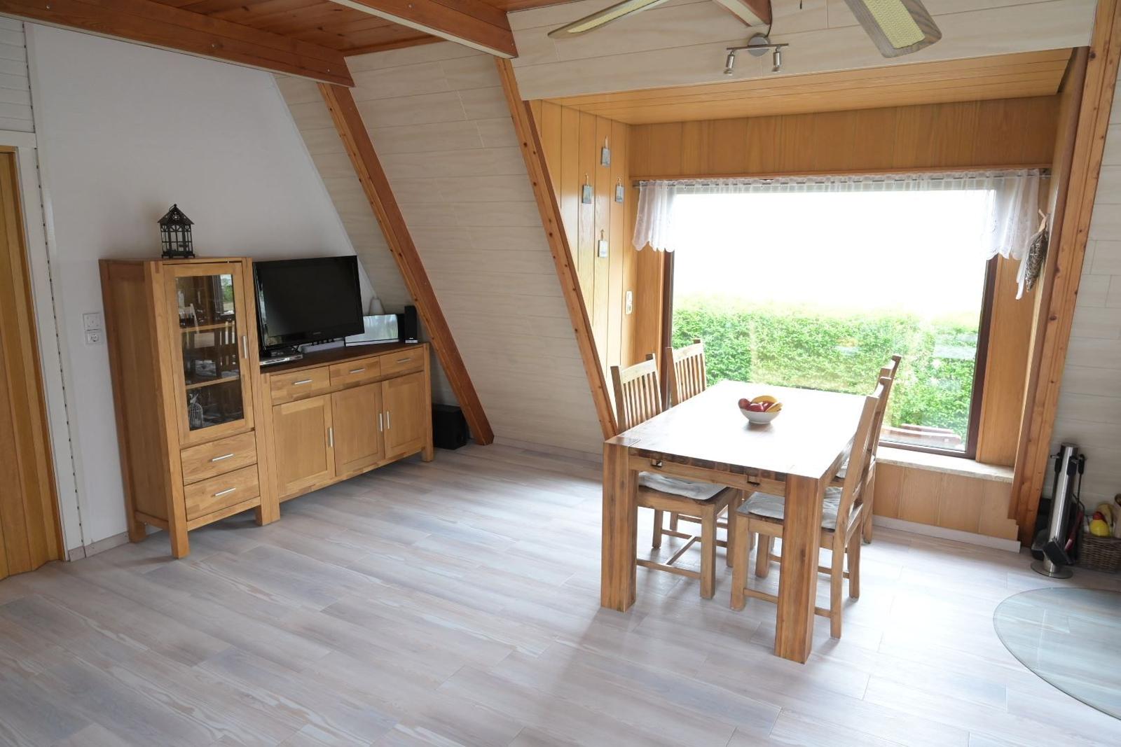 Essbereich mit Holztisch und Stühlen. Fenster mit Blick auf grüne Landschaft.