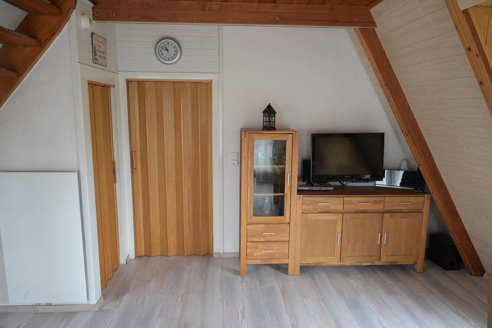 Zimmer mit Holzboden, TV-Möbel und Holztüren unter Dachschräge.