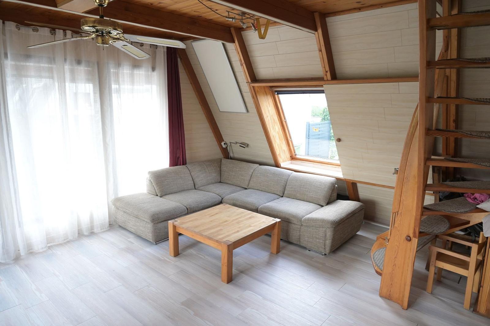 Wohnraum mit Sofa, Tisch und Holzdecke. Fenster und Treppe sind sichtbar.