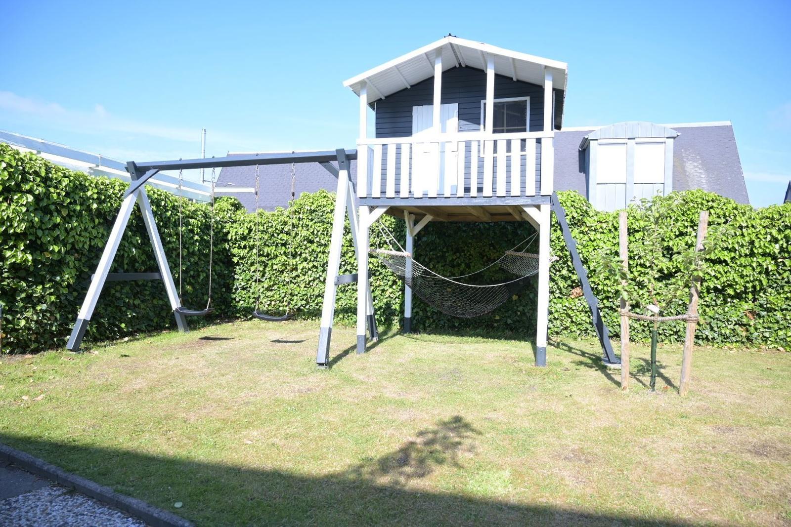 Haus mit Spielplatz, Schaukel und Hängematte im Garten.