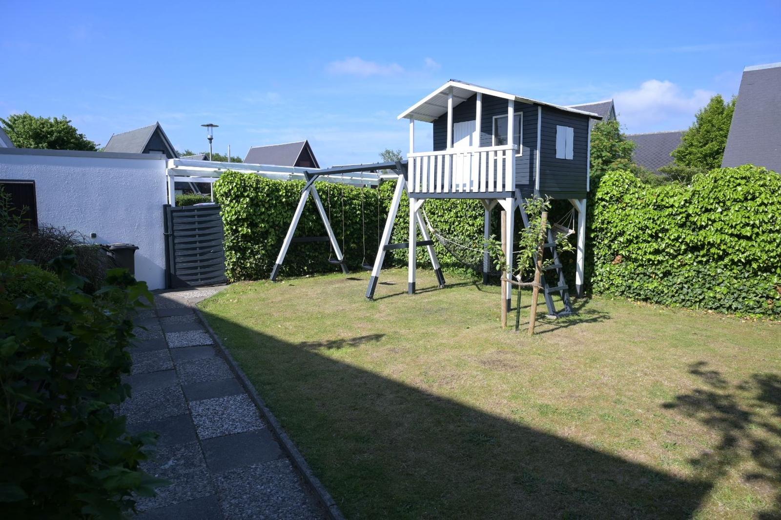 Hinterhof mit Spielhaus, Schaukel und grünem Rasenbereich.