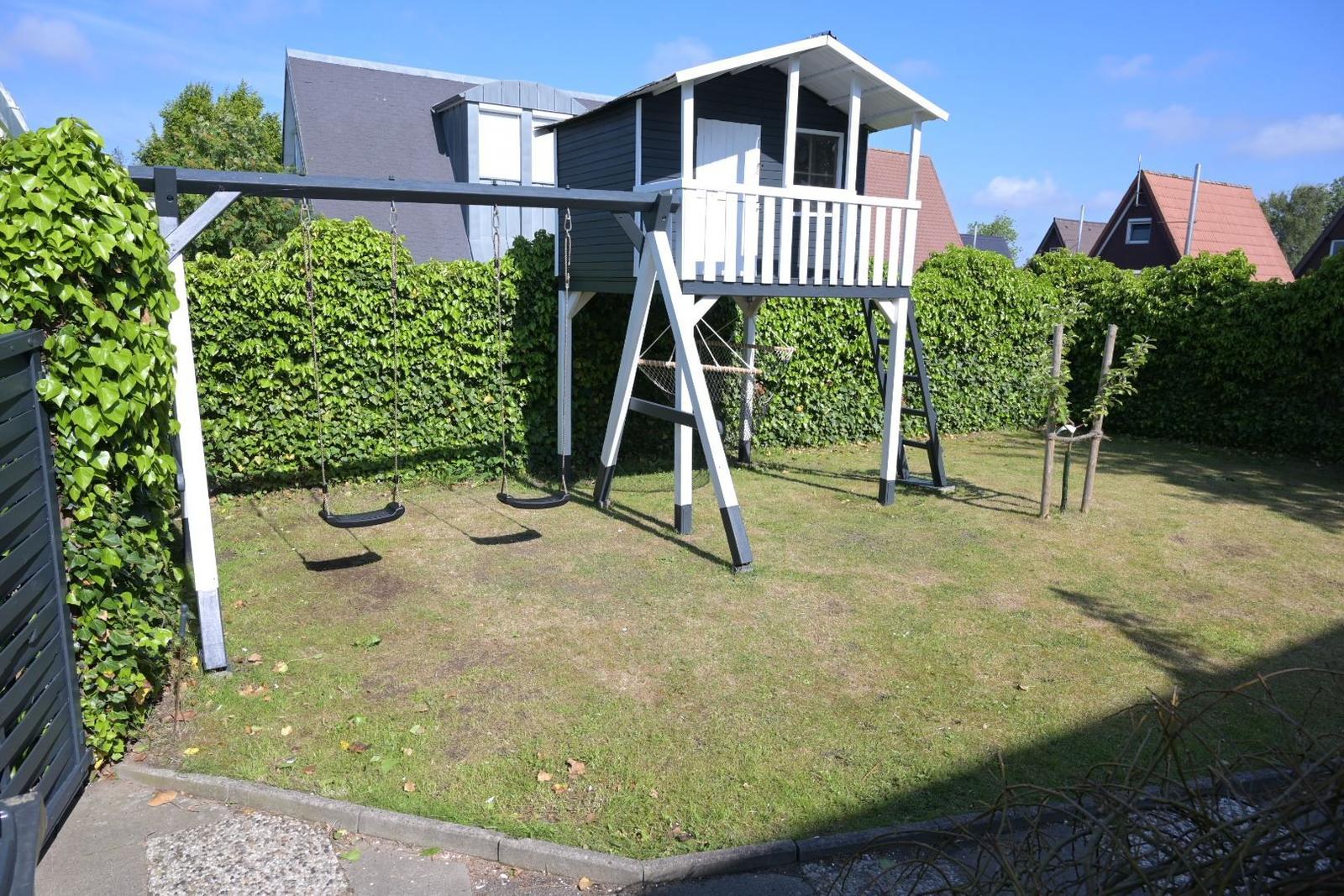 Hinterhof mit Schaukel und Klettergerüst. Grünfläche und Beerenhecke.