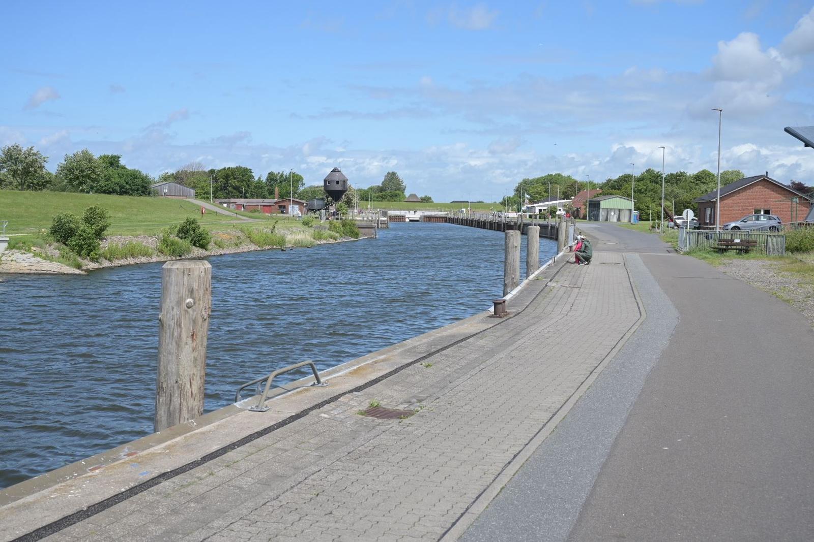 Wasserweg mit Steg, Uferweg und Blick auf Schleusenturm und Grünflächen.