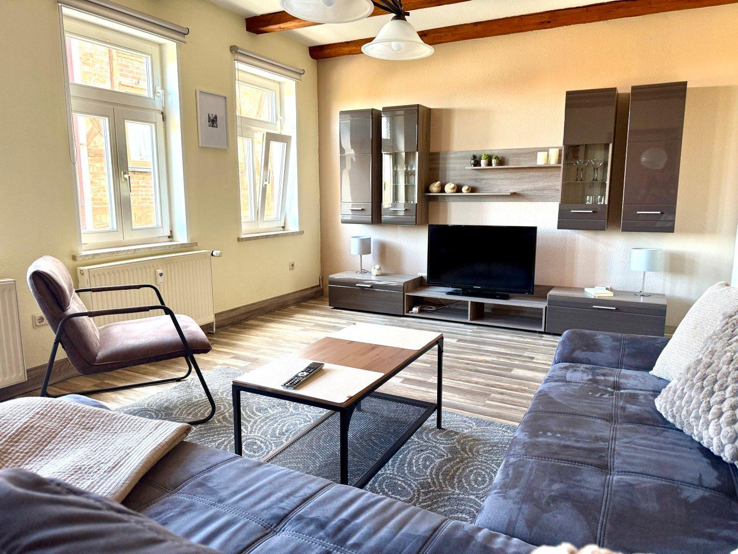 Heller Wohnbereich mit Ecksofa, Ledersessel und Holzbalken - gemütliches Wohnzimmer der Ferienwohnung Harztraum in Blankenburg Harz