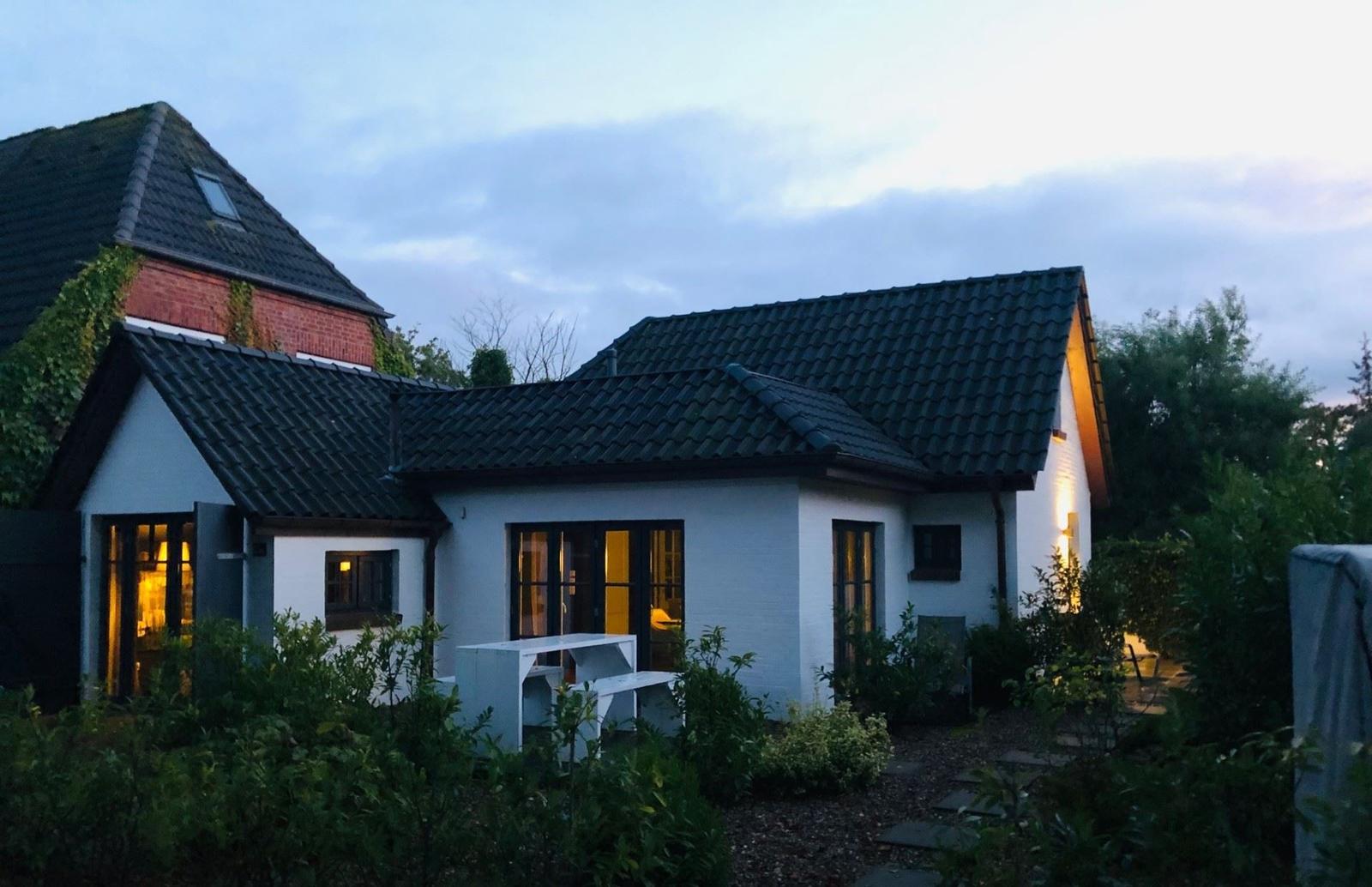 Ein weißes Haus mit schwarzem Dach und beleuchteten Fenstern in einem grünen Garten.