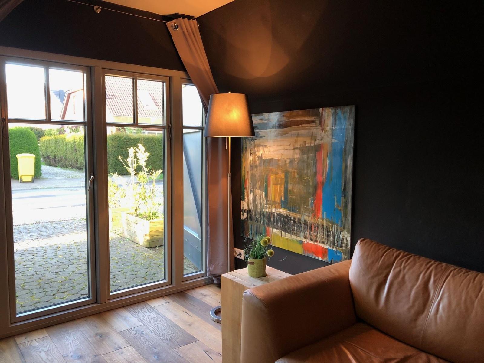 Ein Raum mit braunem Sofa, großer Fensterfront und abstraktem Wandbild.