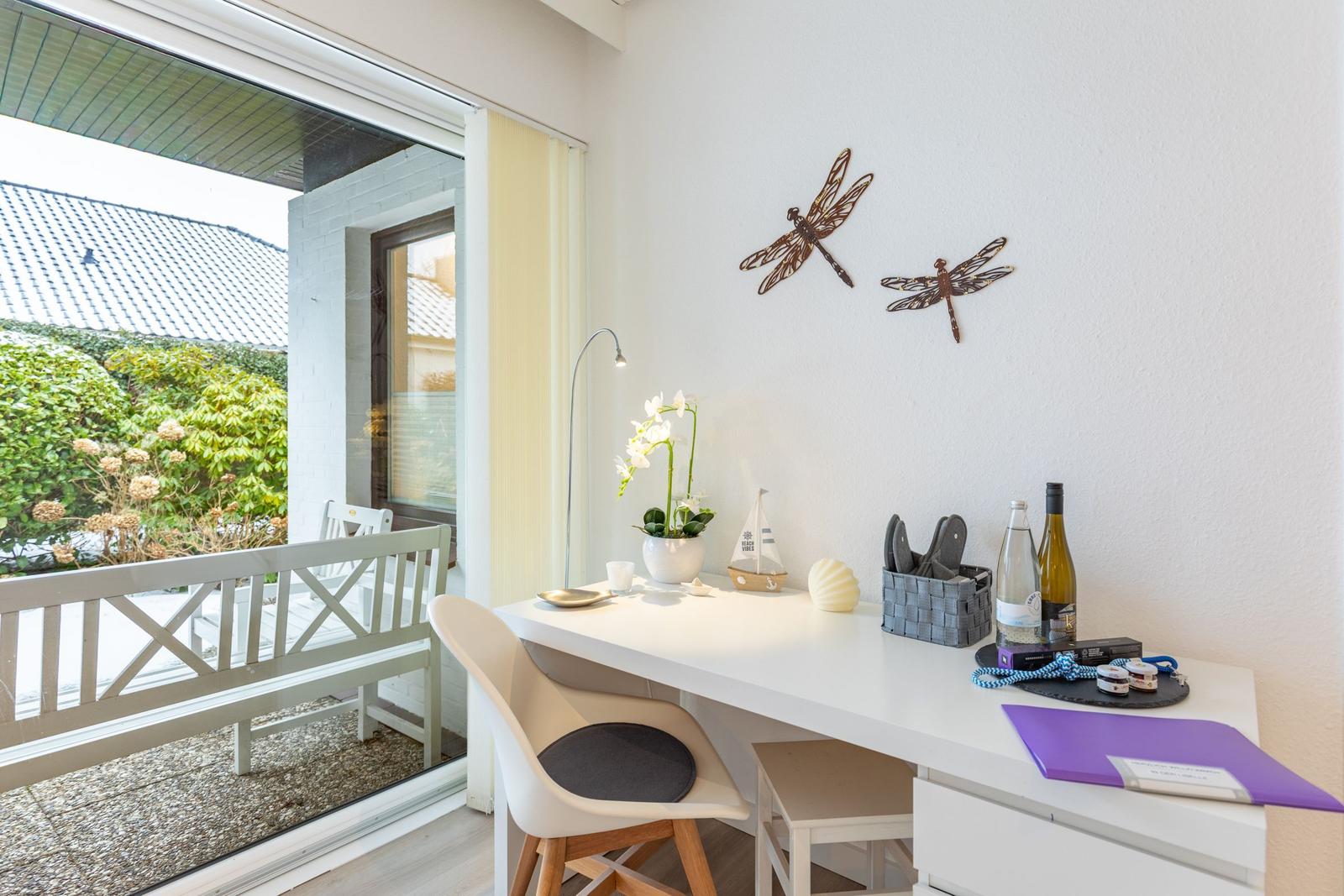 Schreibtisch mit Stuhl und Blick auf Balkon mit Garten.
