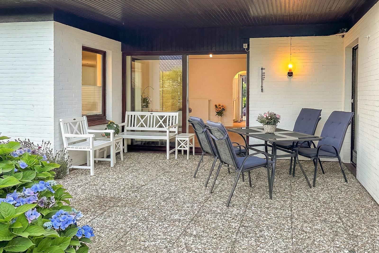 Terrasse mit Sitzgruppe, Tisch und Blumen. Durchgang zur Wohnung.
