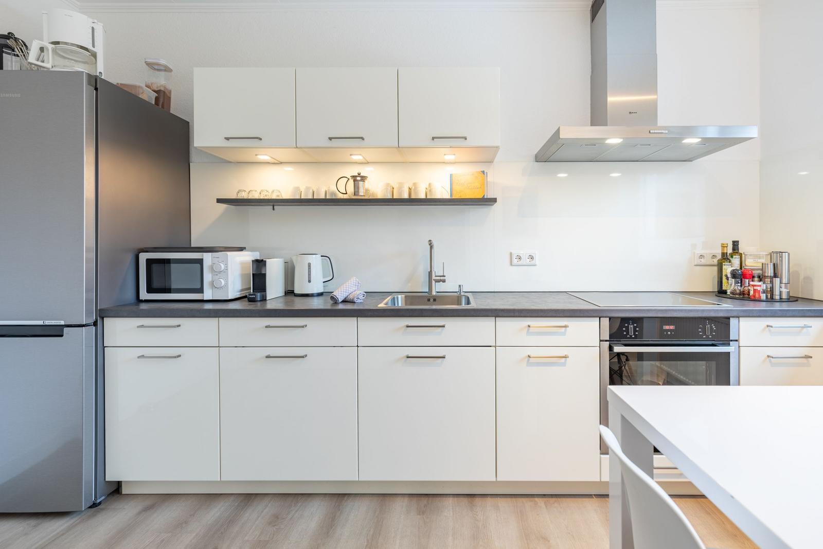 Moderne Küche mit weißen Schränken, Edelstahlgeräten und dunklem Arbeitsplatz.