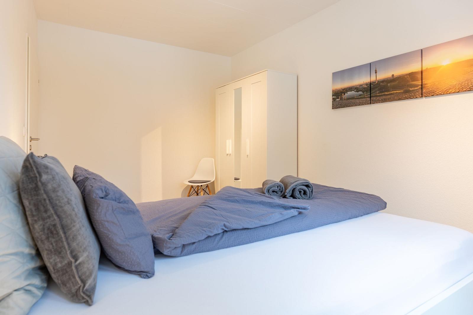Schlafzimmer mit Bett, Kleiderständer und Wandbild.