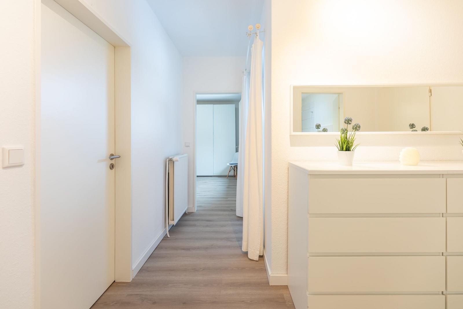 Flur mit Schrank, Spiegel und Heizung. Tür und Vorhang sichtbar.