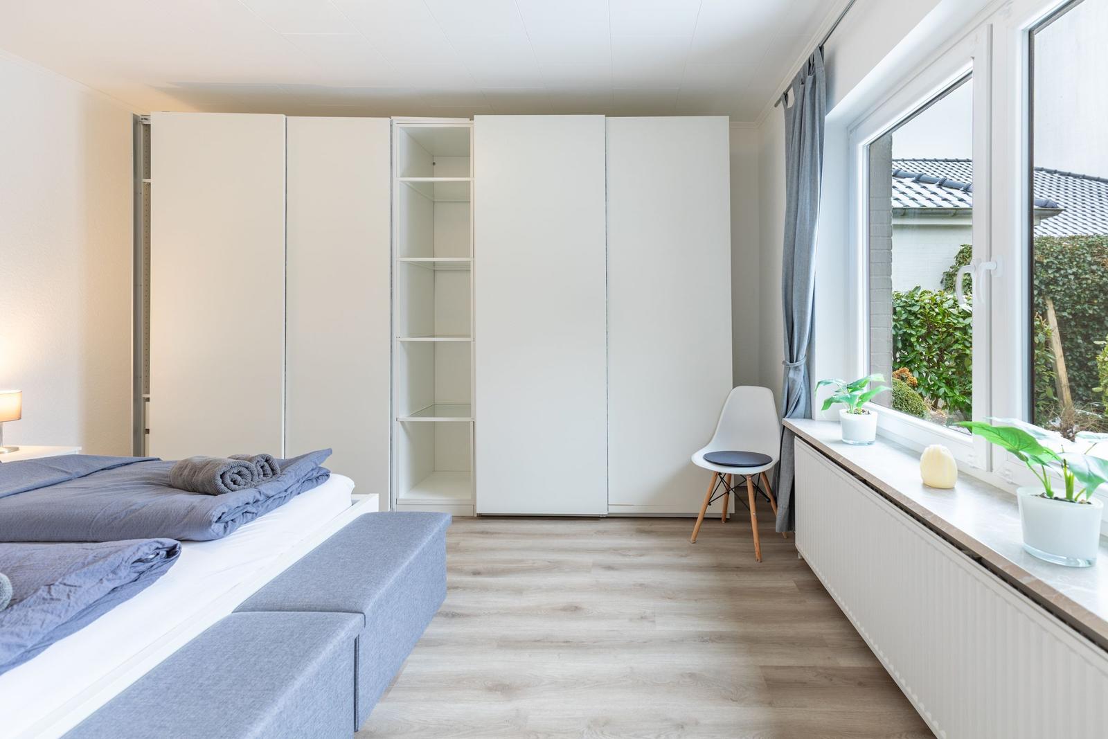 Schlafzimmer mit Bett, Kleiderschrank und Fenster mit Pflanzen.
