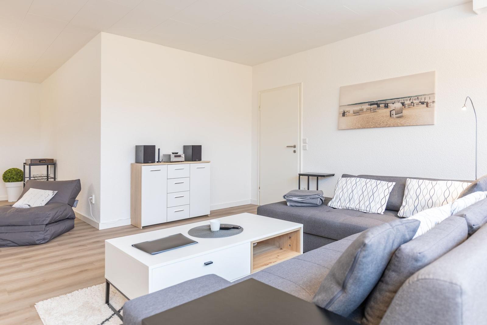 Wohnzimmer mit grauem Sofa, weißen Möbeln und Wandbild.