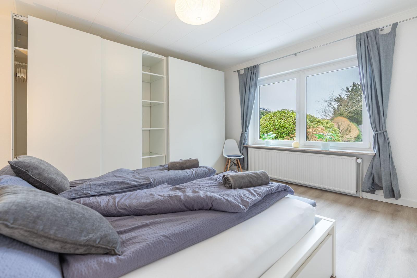 Schlafzimmer mit Doppelbett, Kleiderschrank und Fenster mit Blick auf Garten.
