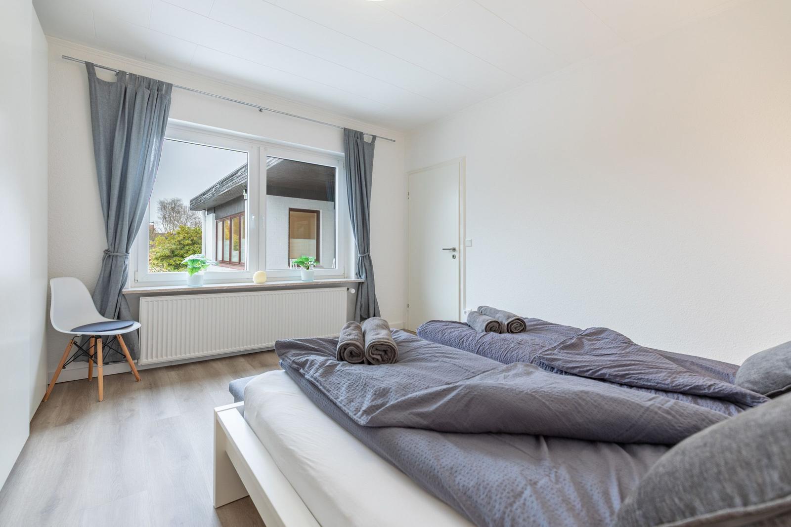 Schlafzimmer mit Doppelbett, Fenster und Stuhl.