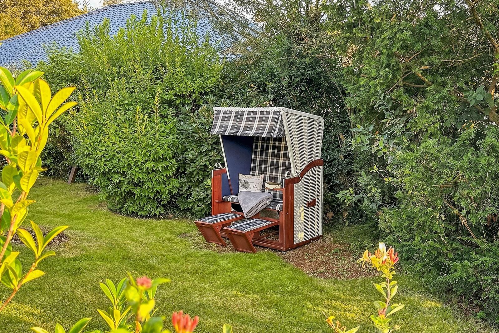Ein Gartenliegestuhl mit gemusterter Plane steht auf einer Wiese zwischen Büschen.