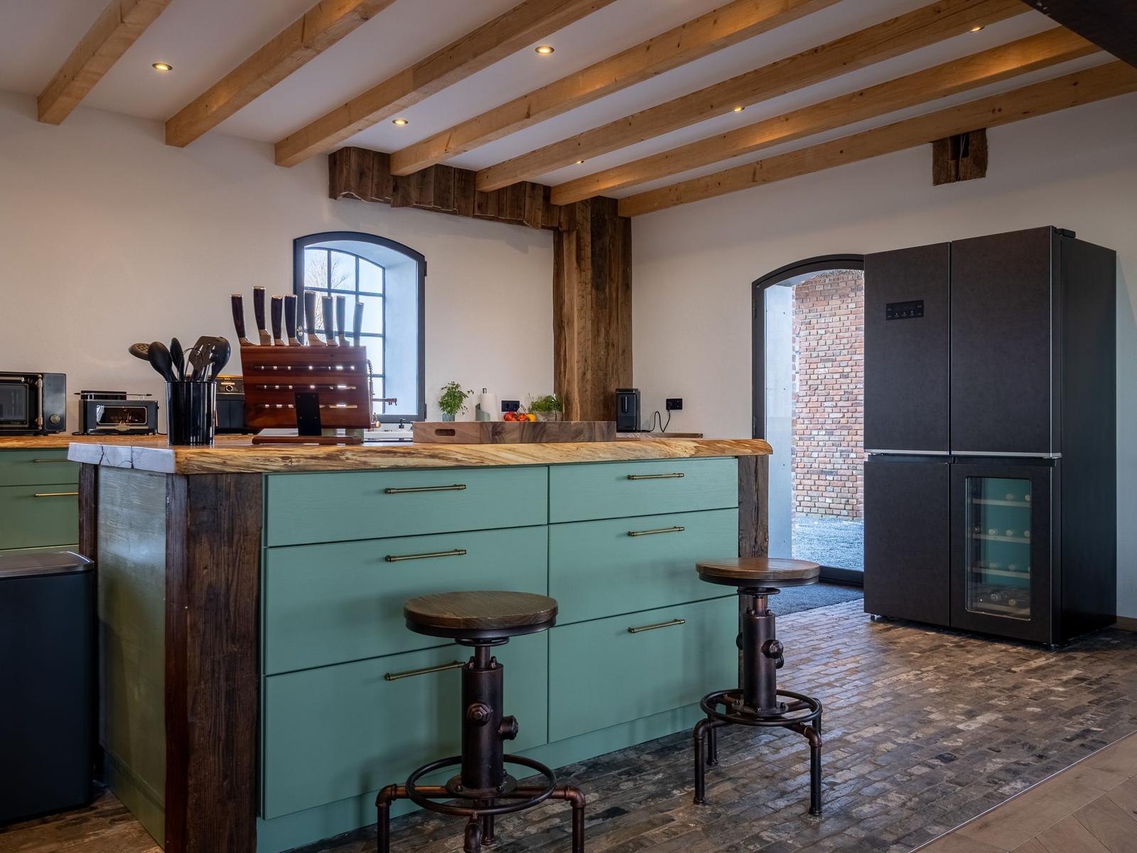 Küche mit Holzbalken, grünen Schränken und schwarzer Kühlschrank