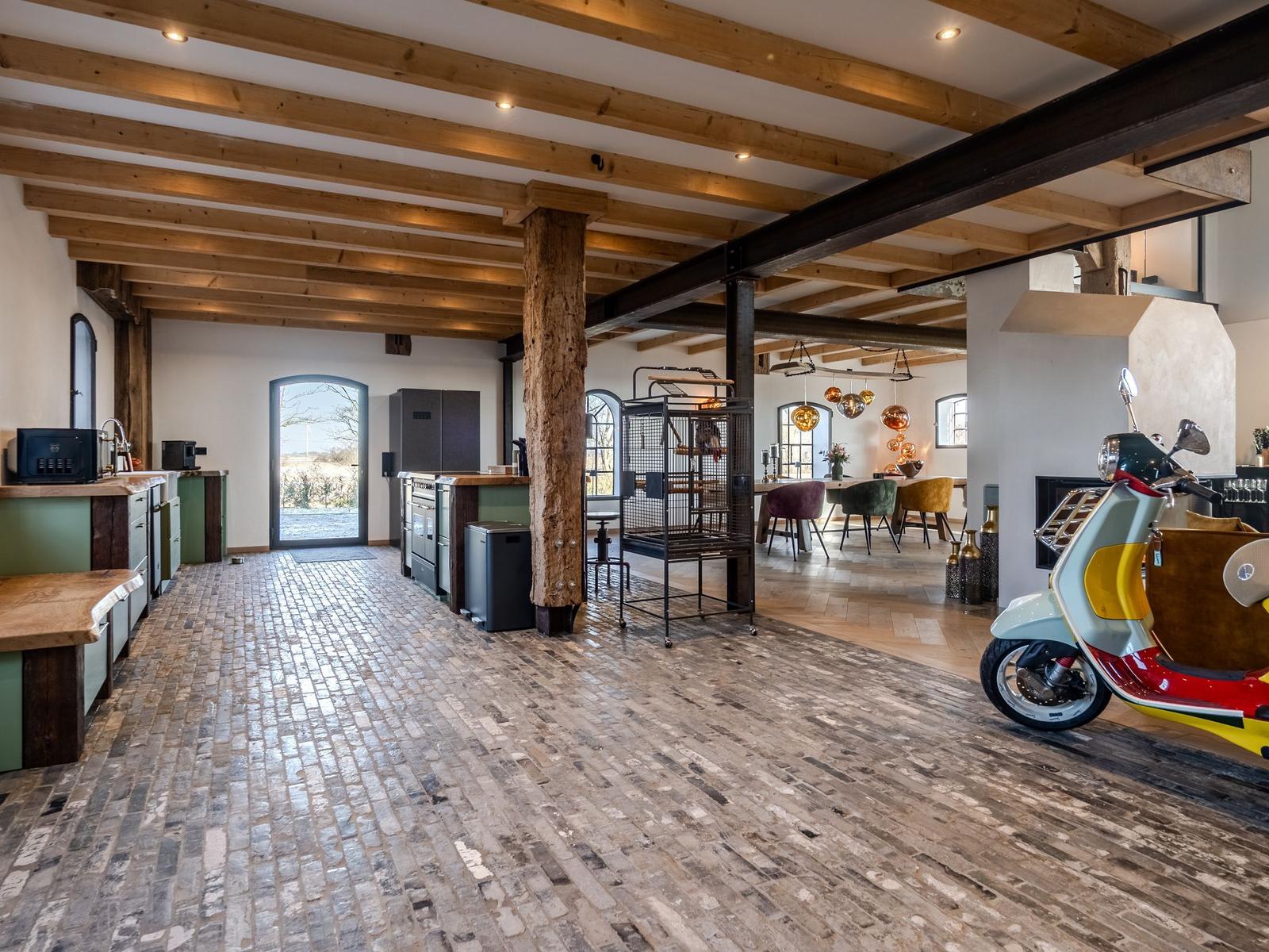 Küche und Essbereich mit Holzbalken und Kachelboden. Ein Scooter steht im Raum.