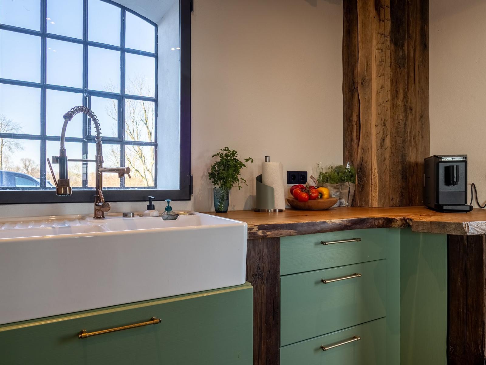 Küche mit grünen Schränken, Holzoberfläche und großem Fenster.