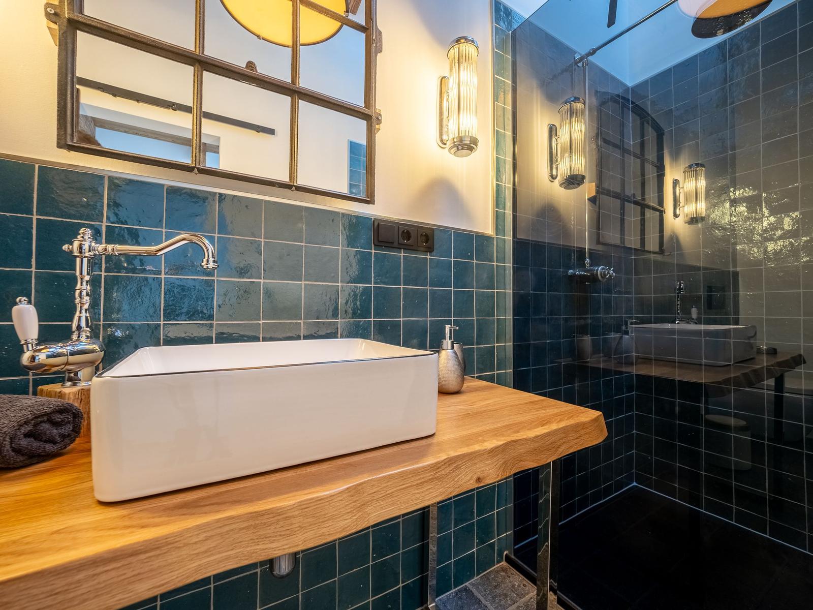 Badezimmer mit Waschbecken auf Holz, blauen Fliesen und Spiegel.