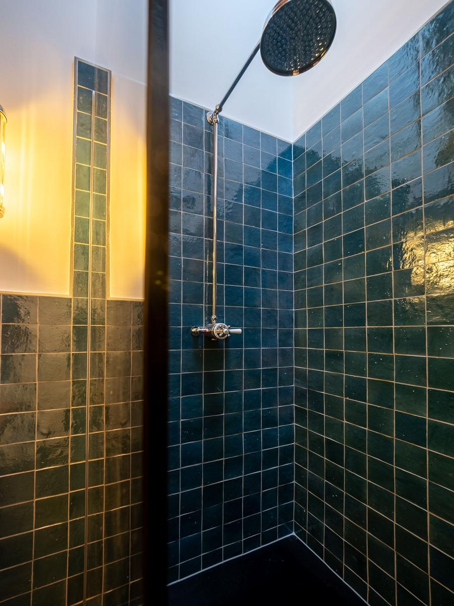 Duschkabine mit dunkelblauen Fliesen und Duschkopf an der Decke.