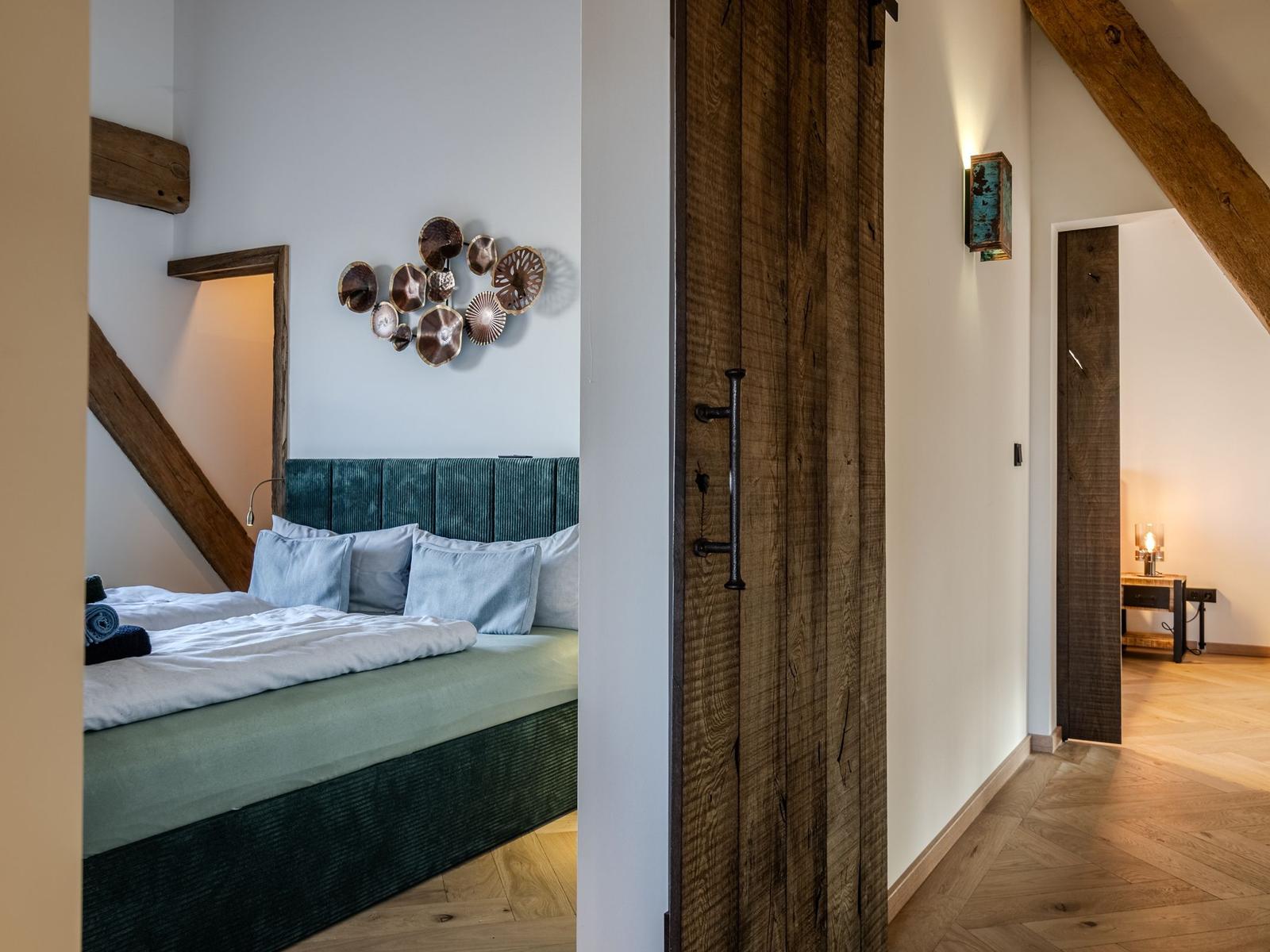 Schlafzimmer mit Bett, Wanddekoration und Holzdeckenbalken. Flur mit Holztür und Boden.