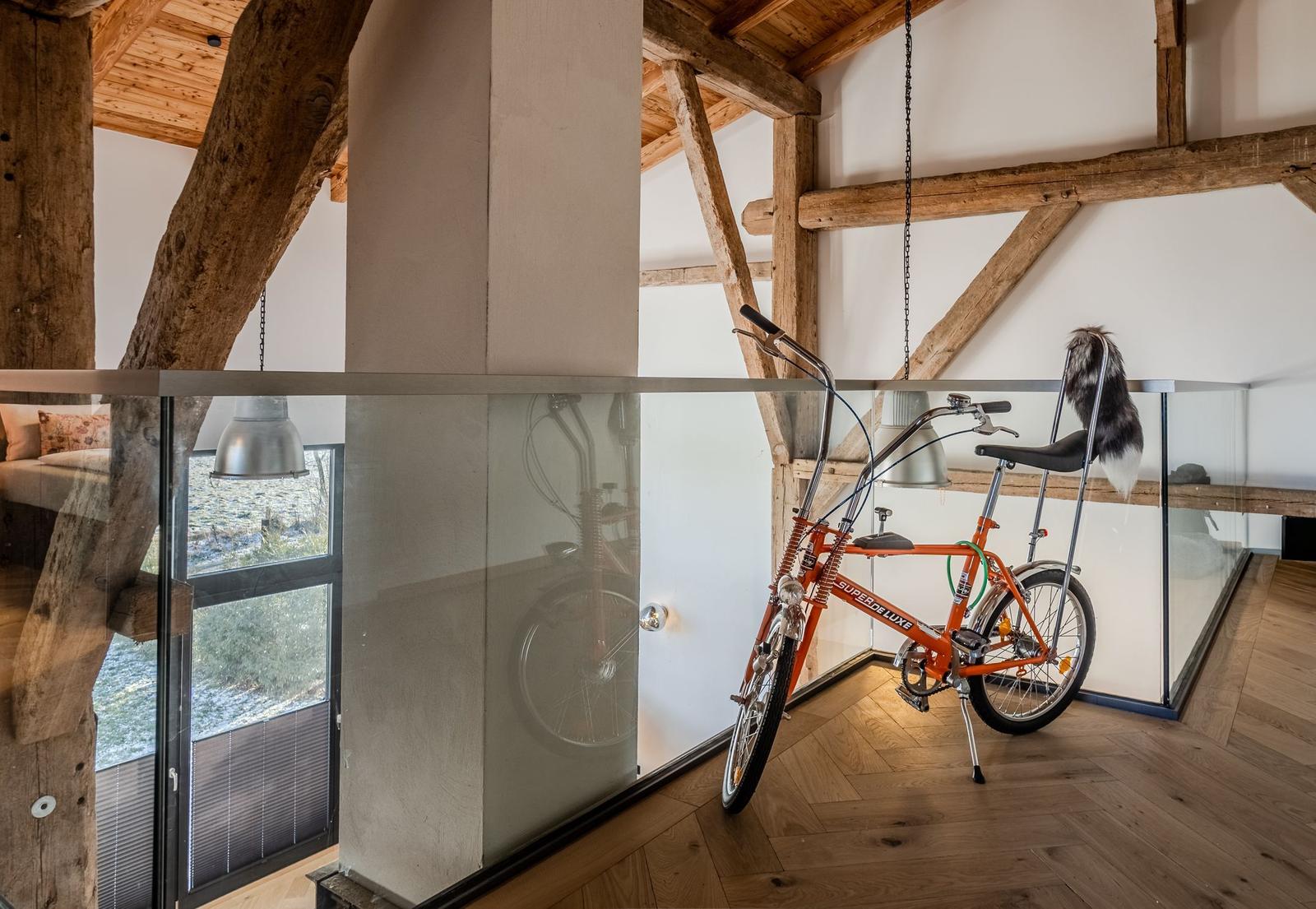 Ein orangefarbener Fahrrad steht in einem Raum mit Holzdecken und Glasgeländer.