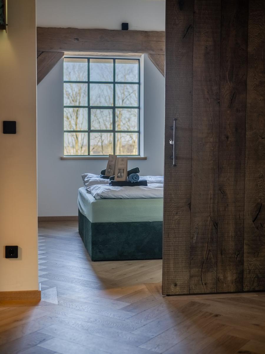 Schlafzimmer mit Bett, Holztür und Fenster mit Blick nach draußen.