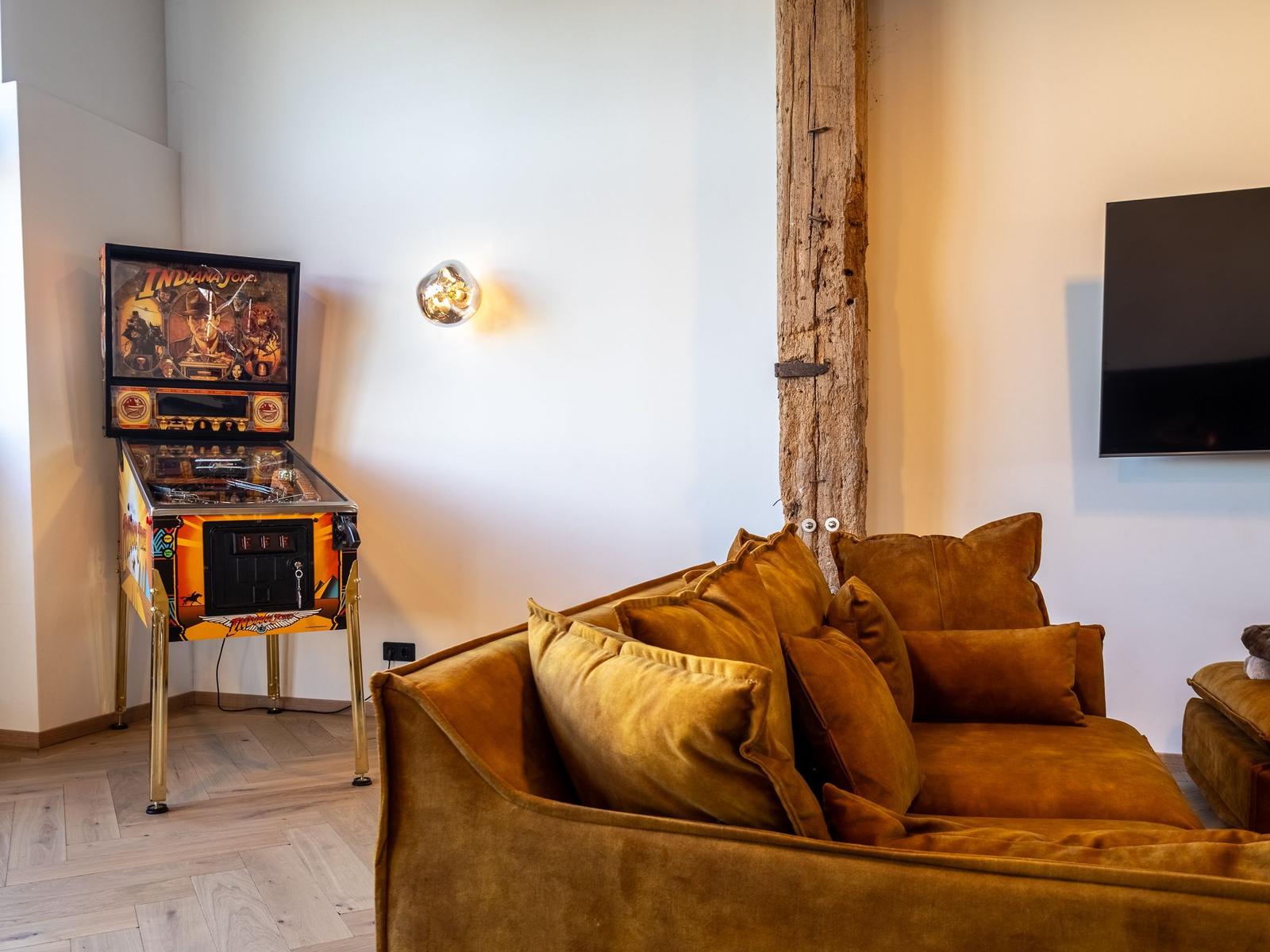 Ein braunes Sofa mit Kissen, eine Pinball-Maschine und eine Wandlampe.