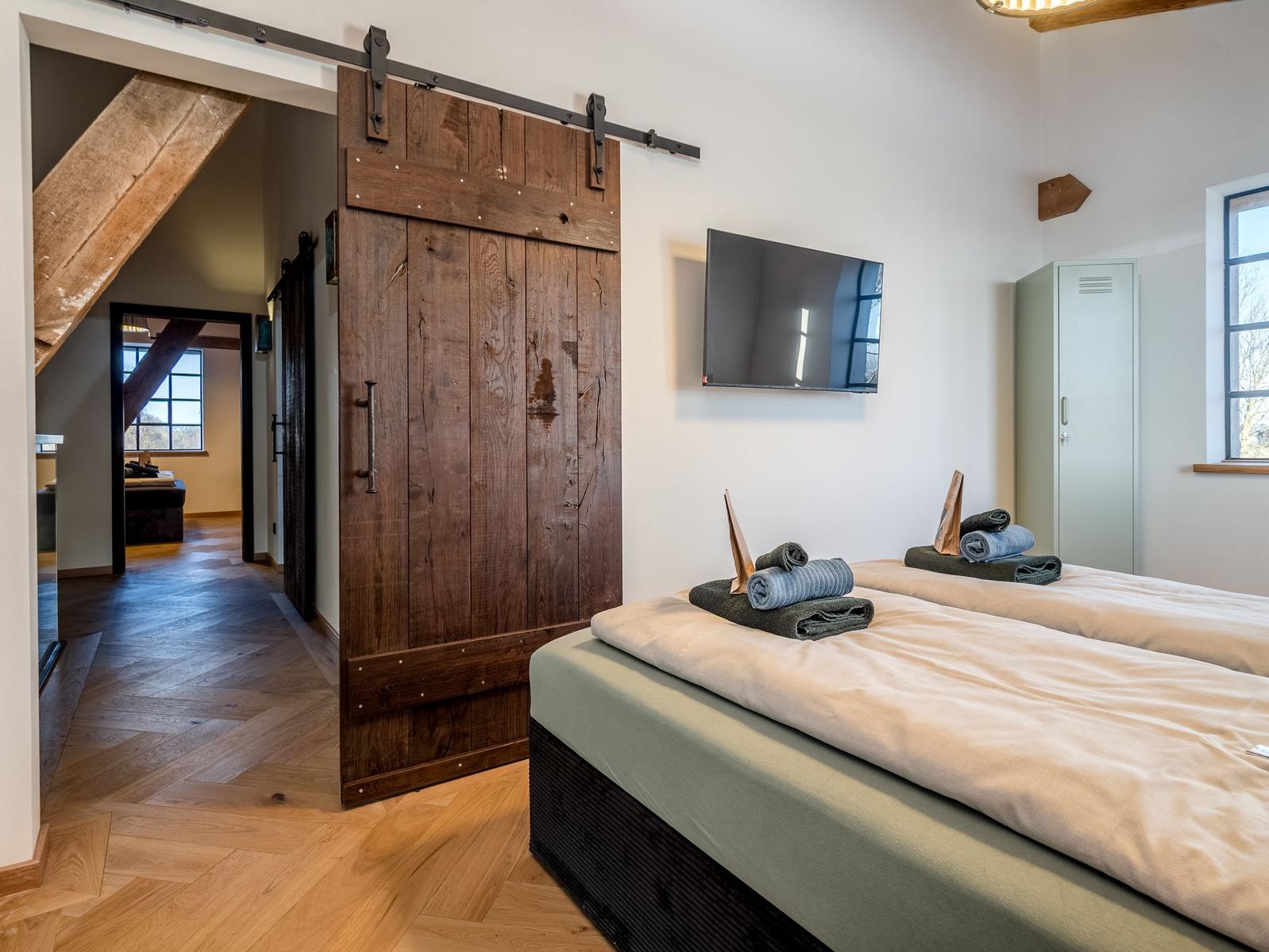 Zwei Betten mit Handtüchern, Holztür und TV an der Wand.