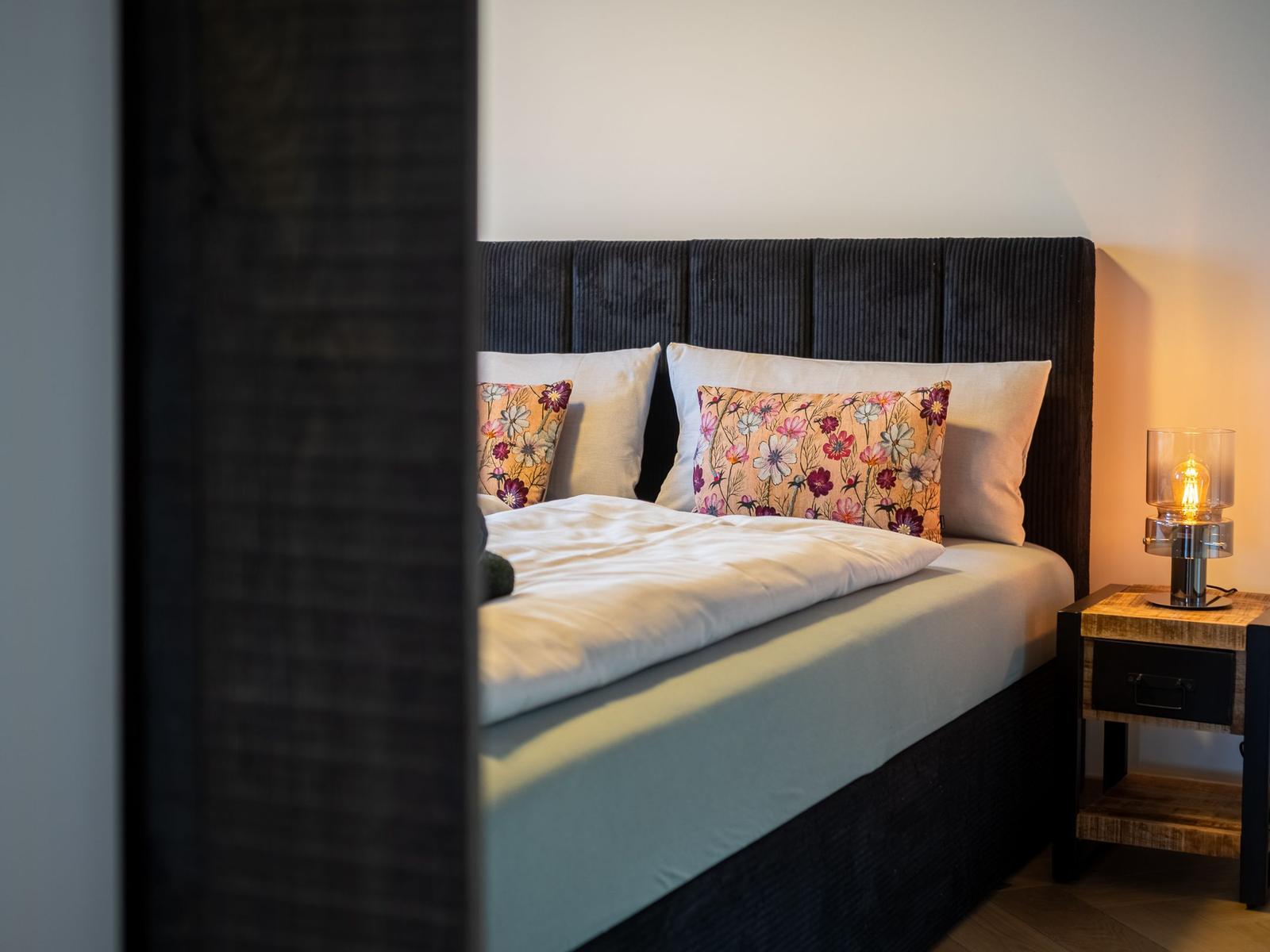 Schlafzimmer mit Bett, Kissen und Nachttisch mit Lampe.