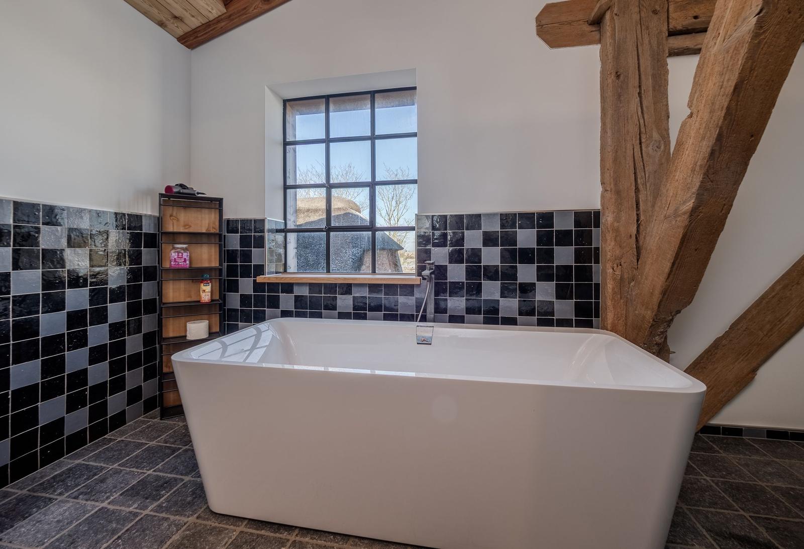 Bad mit freistehender Badewanne, Holzbalken und Fenster mit Blick.