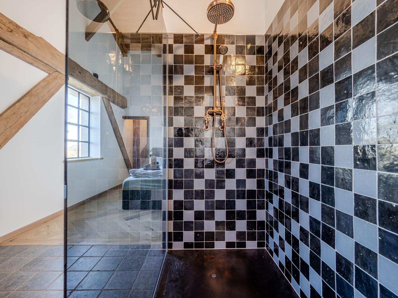 Dusche mit schwarz-weißen Fliesen und Glaswand. Im Hintergrund ein Bett und Fenster.
