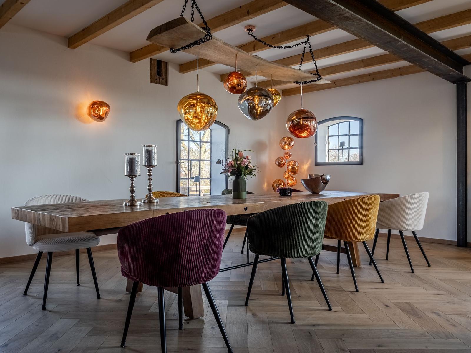 Esszimmer mit Holztisch, bunten Stühlen und hängenden Lampen.