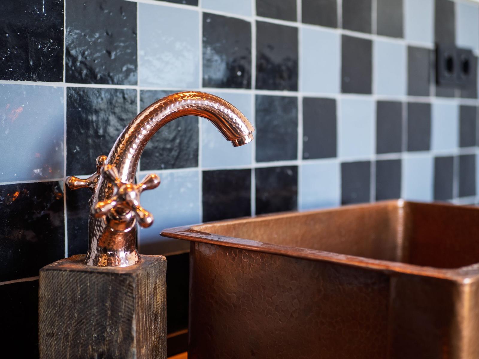 Kupferfarbener Wasserhahn und Waschbecken vor schwarz-weißem Fliesenspiegel.