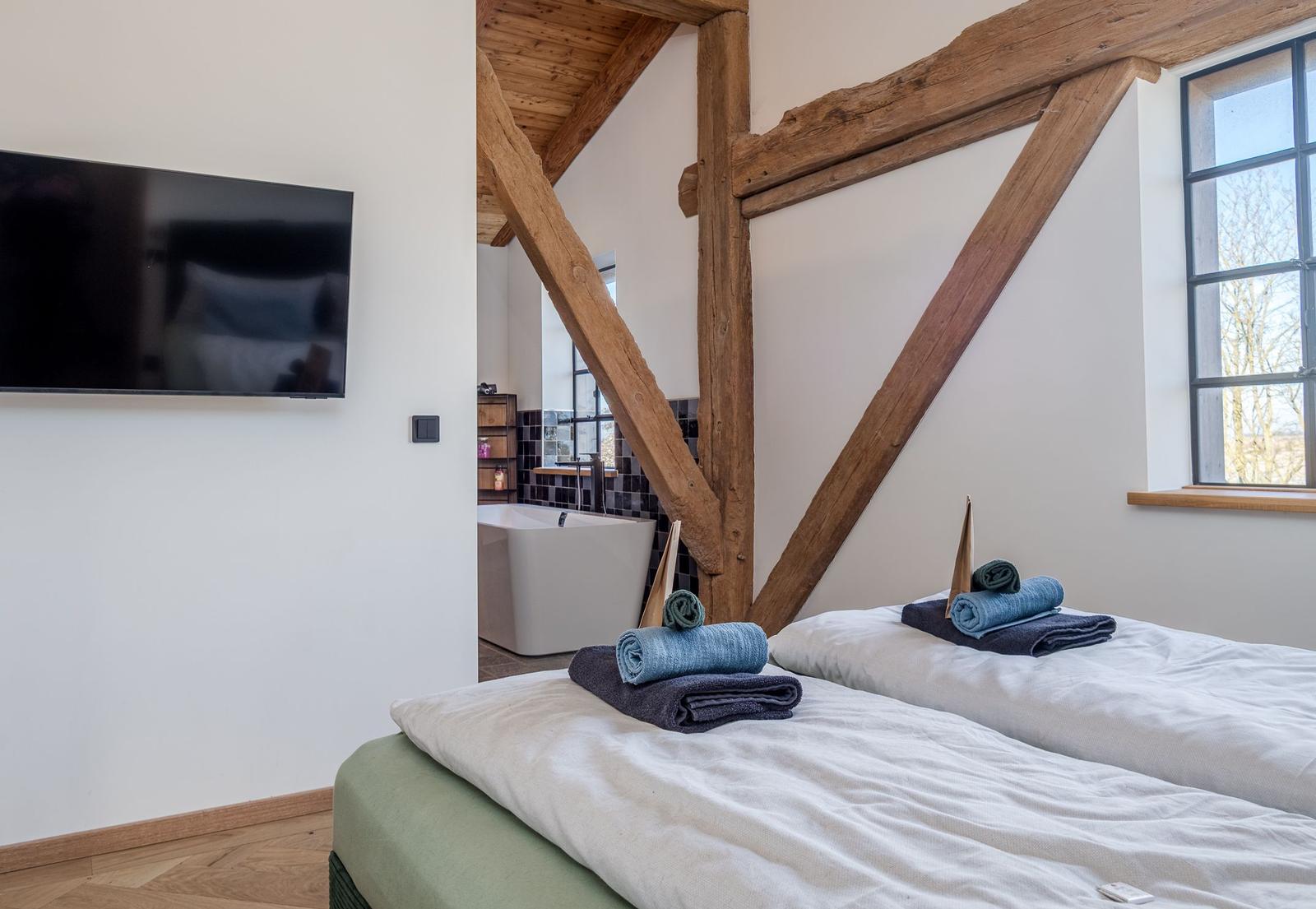 Zwei Betten mit Handtüchern, Holzbalken, Badewanne und Fenster.