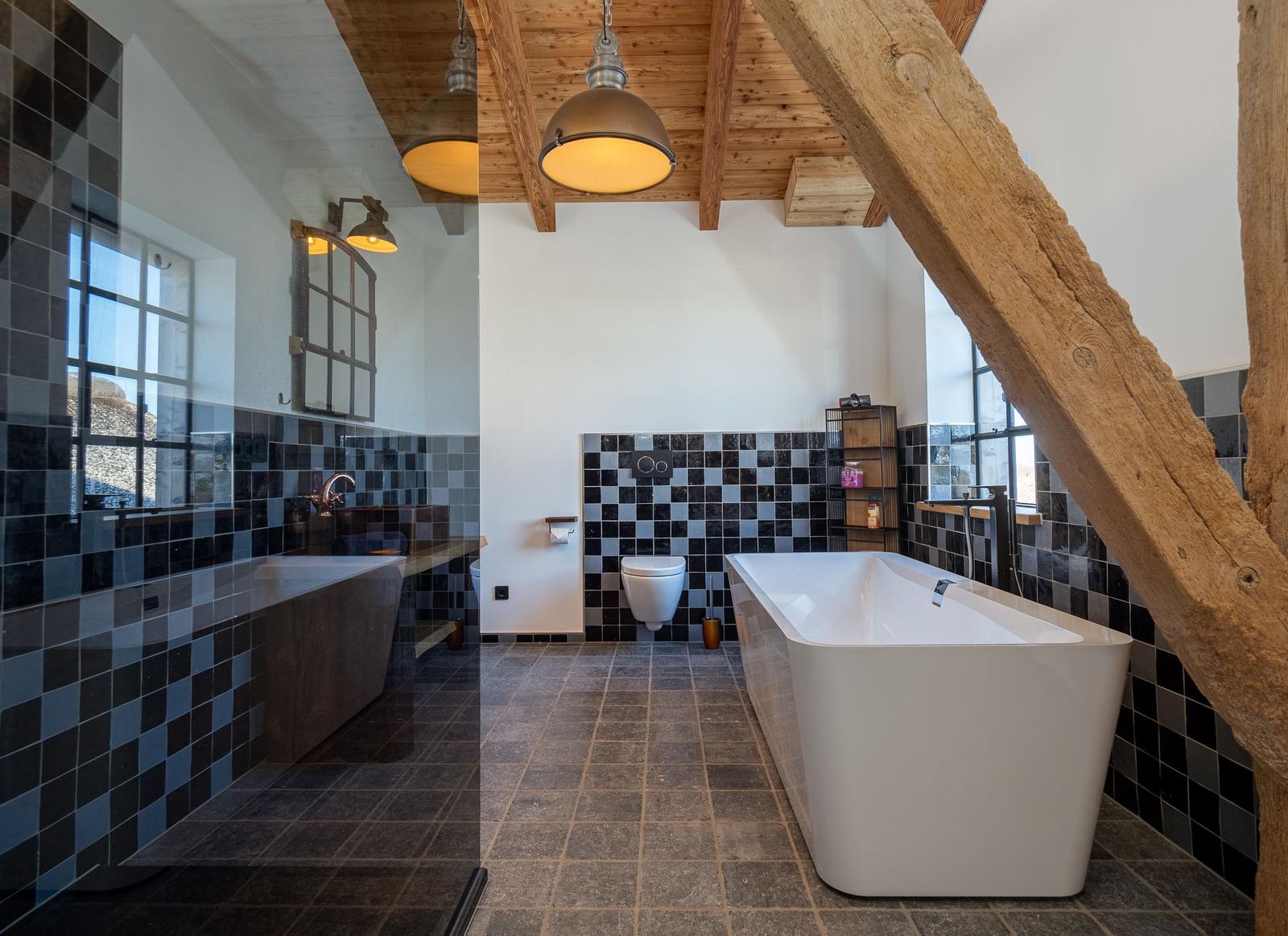 Badezimmer mit freistehender Badewanne, Holzbalken und schwarz-weißen Fliesen.