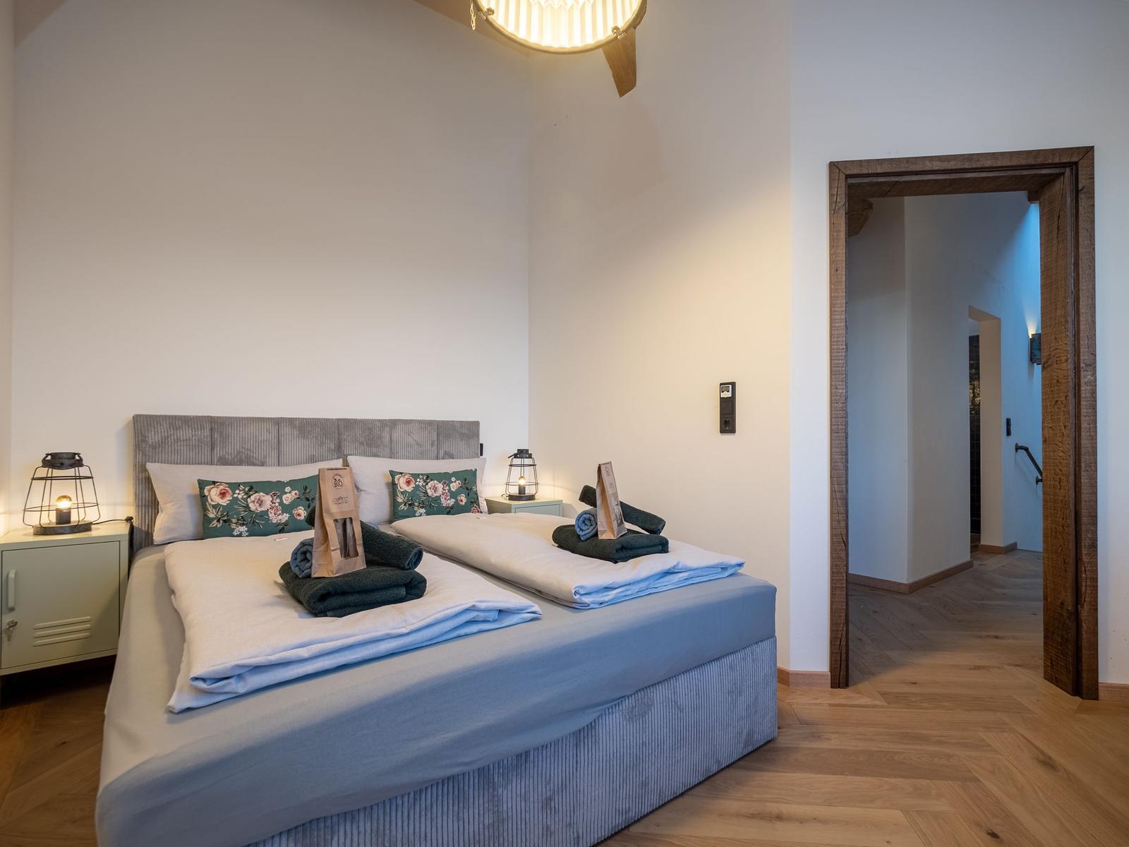 Schlafzimmer mit Doppelbett, Holzboden und Tür zum Flur.