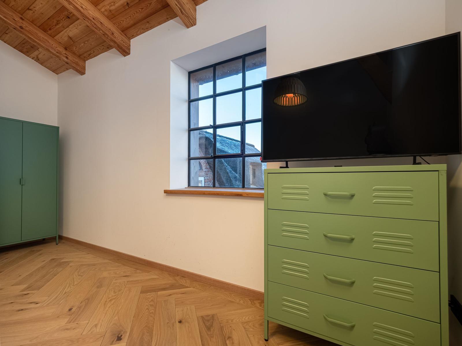 Zimmer mit grünem Schrank, Holzboden und TV auf Schrank.