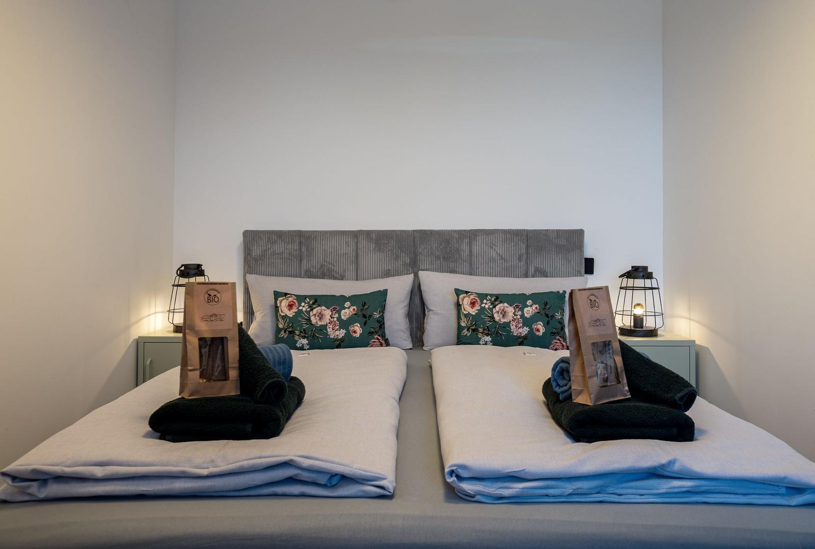 Doppelbett mit Kissen, Handtüchern und Bio-Kaffeebeuteln auf Nachttischen.