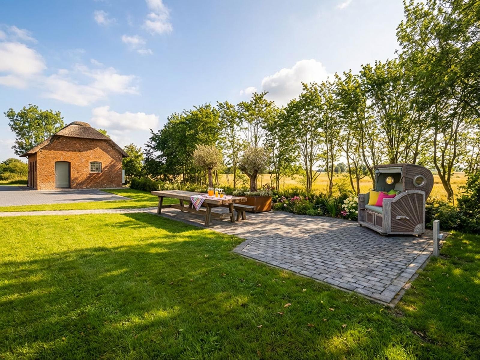 Haus mit strohgedecktem Dach, Terrasse mit Tisch, Bänken und Sitzmöbeln im Garten.